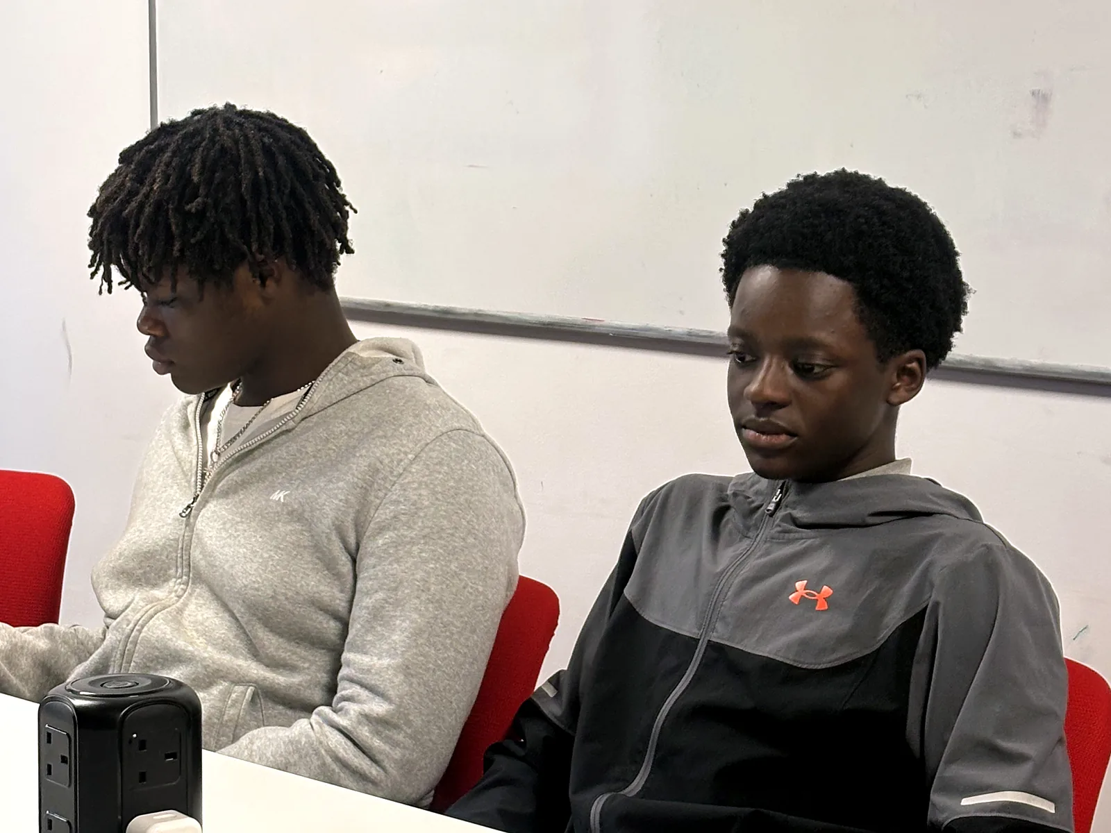 Two young people sitting at a table in front of a whiteboard during a JDS session